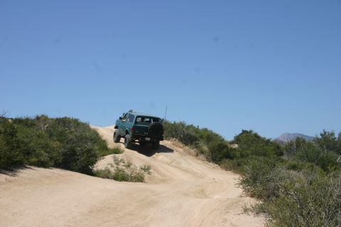 1991 Ford Bronco - A green 1991 Ford Bronco navigates an off-road trail under a clear blue sky.