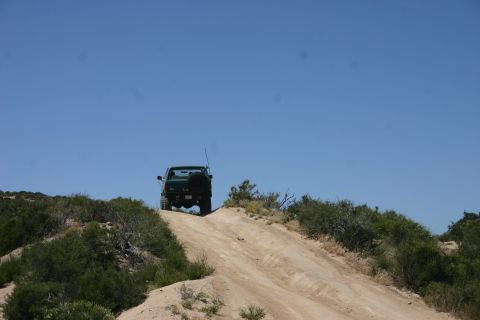 1991 Ford Bronco - A green 1991 Ford Bronco ascends a dusty incline under a clear blue sky.