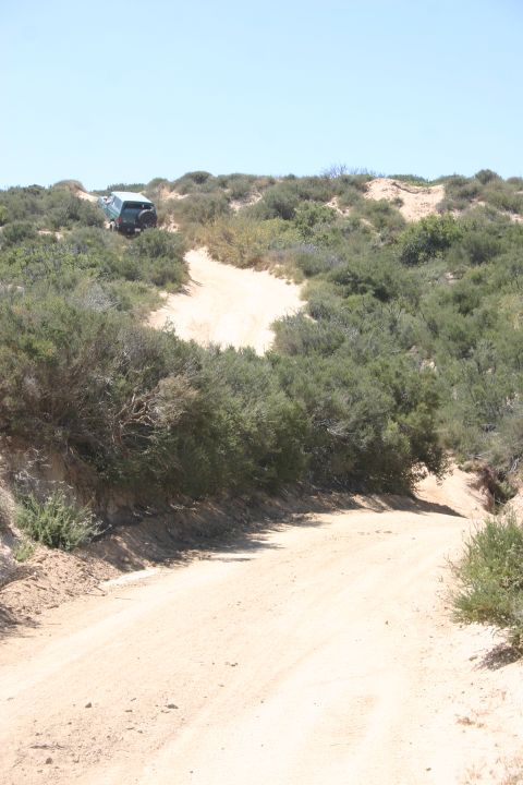 1991 Ford Bronco - An SUV navigates a dirt path through a scrub-covered, hilly landscape under a clear blue sky.
