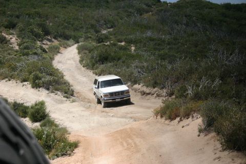 1991 Ford Bronco - A white Ford Bronco navigates a rough dirt track in a dry, hilly landscape.
