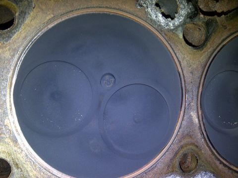 1986 Ford Bronco - Close-up view of an engine cylinder head showing two valve openings and signs of carbon buildup.