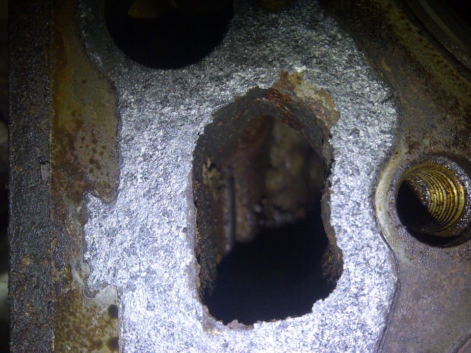 Close-up of a heavily corroded metal engine component with a large hole