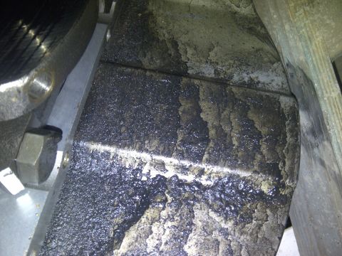 1986 Ford Bronco - Close-up view of a heavily soiled engine oil pan, indicating significant wear and tear.