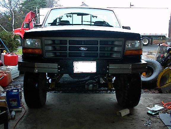 Front view of a lifted white Ford pickup with black grille and large tires in a driveway