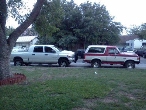 1989 Ford Bronco - Two vehicles parked curbside: a red and white Ford Bronco and a white pickup truck.