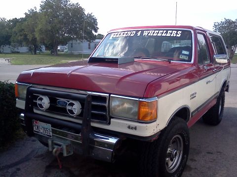1989 Ford Bronco - This 1989 Ford Bronco features a two-tone red and white paint scheme, a prominent hood scoop, and auxiliary off-road lighting on the front…