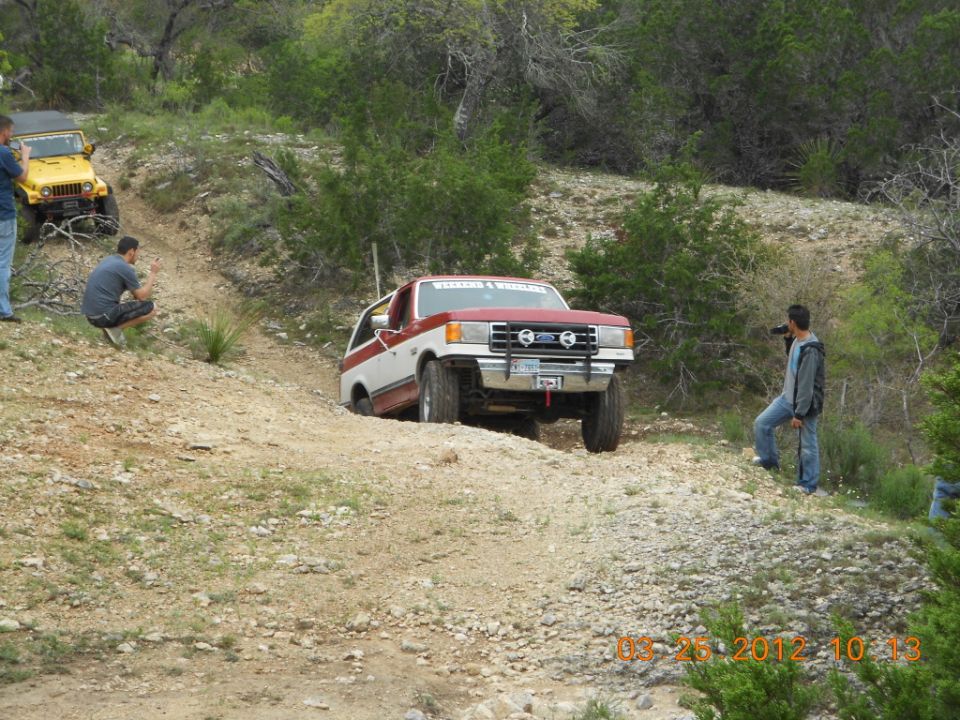Red and white Ford Bronco climbing a dirt hill, yellow Jeep behind it