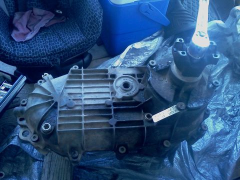 1989 Ford Bronco - A dirty transfer case sits on a tarp, with a seat and blue container in the background.