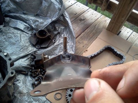 1989 Ford Bronco - Disassembled vehicle parts including a metal bracket and a roller chain are laid out on a wooden surface.