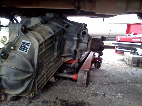 1989 Ford Bronco - A vehicle transmission is being supported by a red hydraulic jack underneath a vehicle.