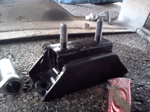 1989 Ford Bronco - A black engine mount with two threaded studs is shown on gravel, with a socket wrench nearby.