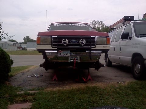 1989 Ford Bronco - Front view of a maroon Ford truck with its front wheels off, parked next to a white van.