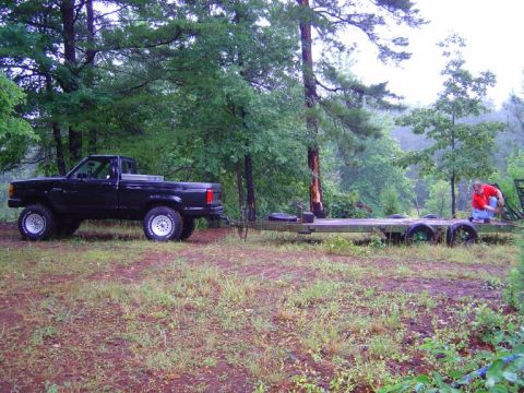 1989 Ford Ranger - A black pickup truck tows a flatbed trailer through a wooded area.