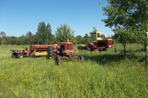 1987 Ford F-250 - Farm equipment including an ATV, baler, tractor, and combine sits in a field of grass and yellow flowers.