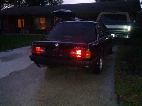 1991 BMW 3 Series - A dark BMW 325i is parked in a driveway, with another vehicle visible behind it.