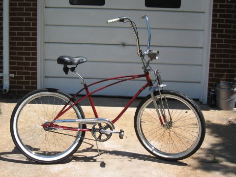 1994 Ford Bronco - A red cruiser bicycle with chrome accents and whitewall tires is parked outside a garage.