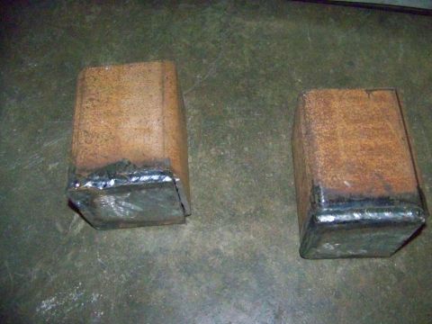 1985 Ford Bronco - Two custom-fabricated metal blocks, likely for a vehicle modification, sit on a concrete floor.