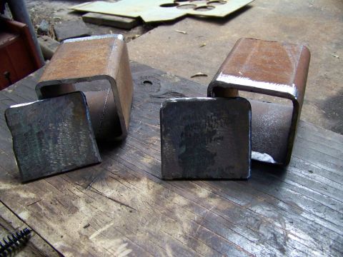 1985 Ford Bronco - Two fabricated metal components rest on a weathered wooden surface, with a brush visible in the lower left corner.