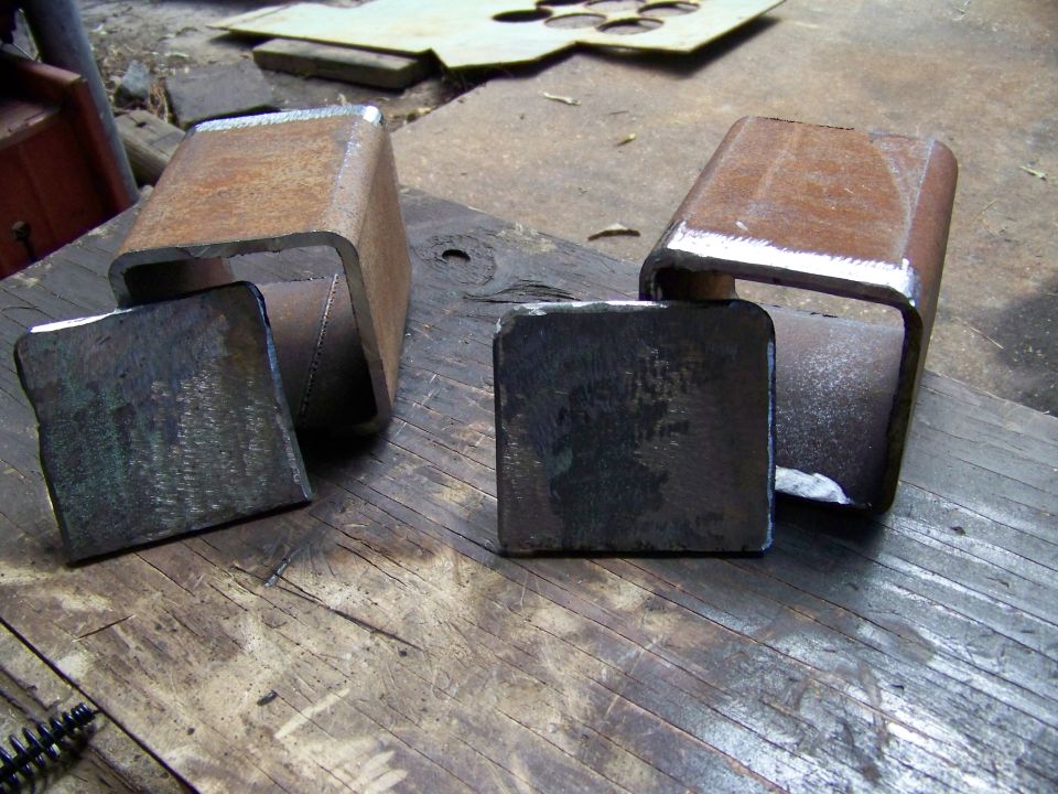 Two metal U-shaped parts and two square metal plates on a wooden workbench
