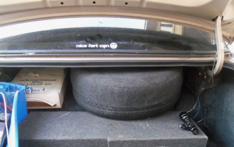 2000 Mercury Grand Marquis - The trunk of a car contains a spare tire, a spill clean-up kit, and a humorous sticker on the rear window.