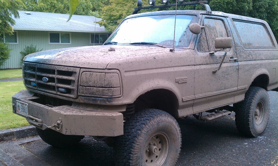 Mud-covered 1995 Ford Bronco with off-road tires and custom bumper parked in front of a house.