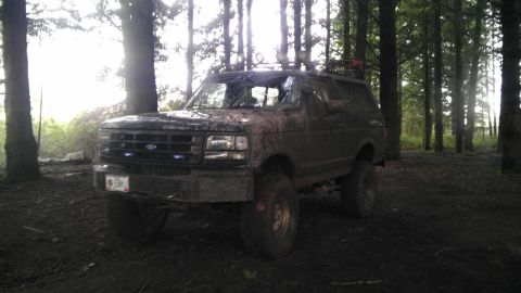 1995 Ford Bronco - Muddy 1995 Ford Bronco off-roading in a dense forest setting.