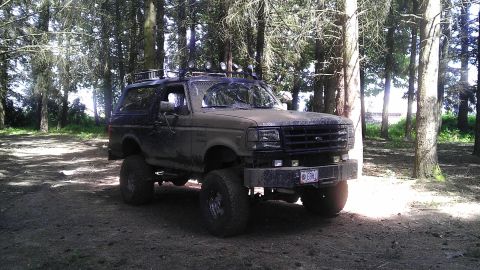 1995 Ford Bronco - Modified 1995 Ford Bronco with off-road tires sits in a forest clearing.
