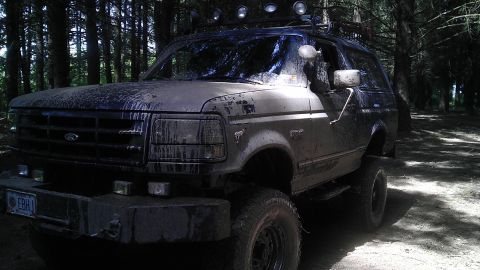 1995 Ford Bronco - This heavily muddied Ford Bronco is seen from a 3/4 front angle in a wooded area.