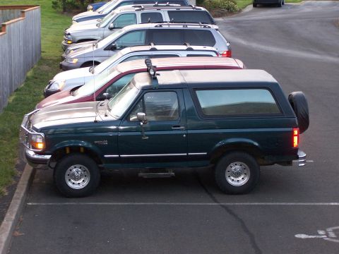 1995 Ford Bronco - A dark green Ford Bronco is parked in a lot next to other vehicles.
