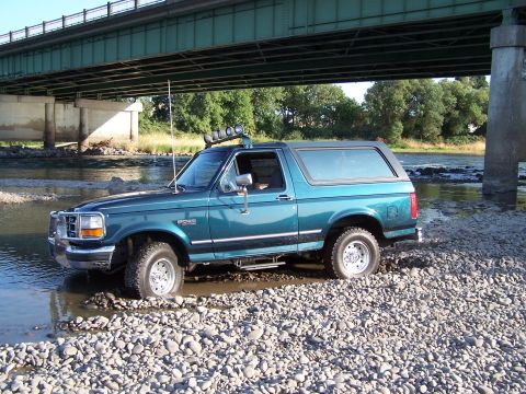 1995 Ford Bronco - This 1995 Ford Bronco navigates a shallow riverbed, its off-road capabilities evident under a large bridge.