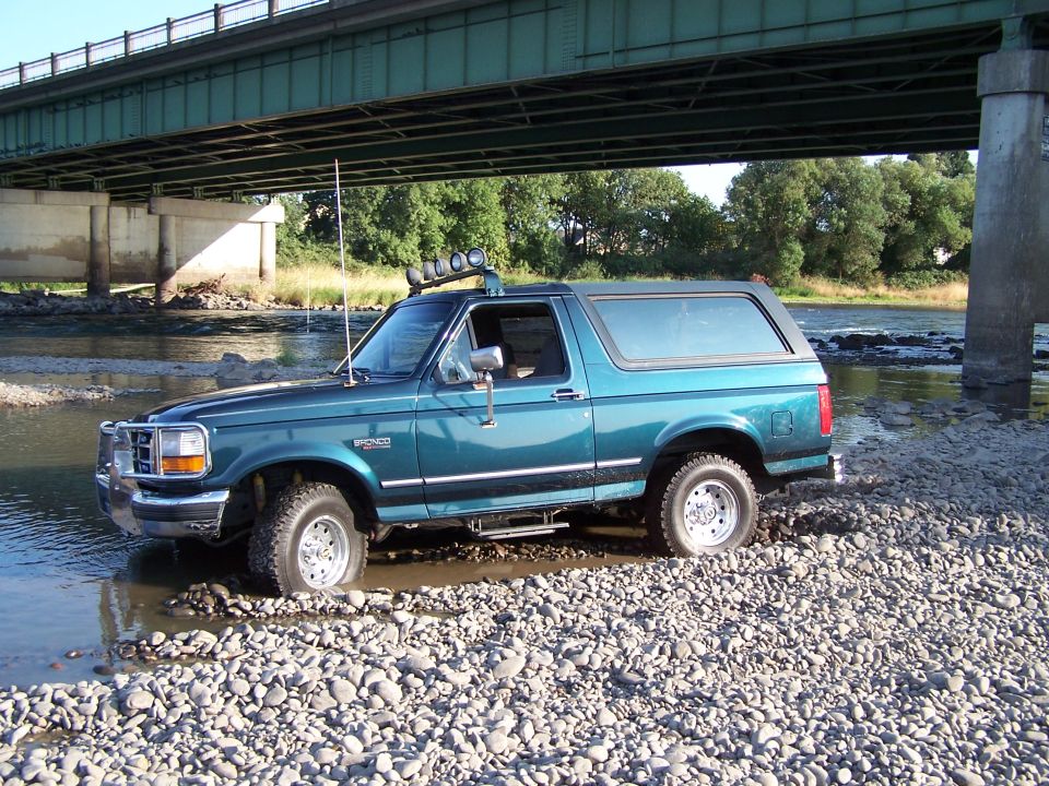 Teal 1995 Ford Bronco with roof lights driving through a rocky riverbed