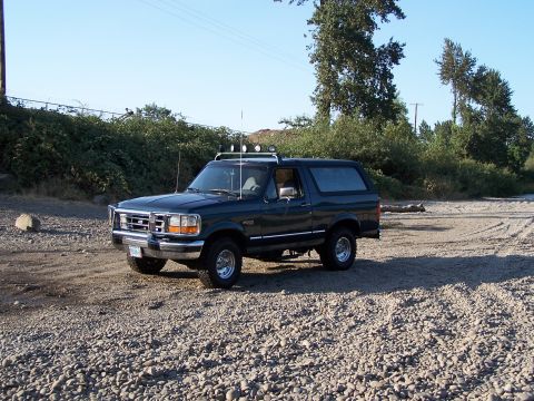 1995 Ford Bronco - Dark green 1995 Ford Bronco with roof-mounted lights sits on a rocky lot under a clear sky.