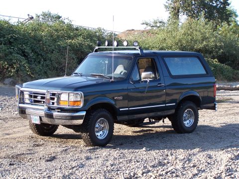1995 Ford Bronco - This dark green Ford Bronco SUV, seen from a 3/4 front angle, is equipped with a roof rack and spotlights.