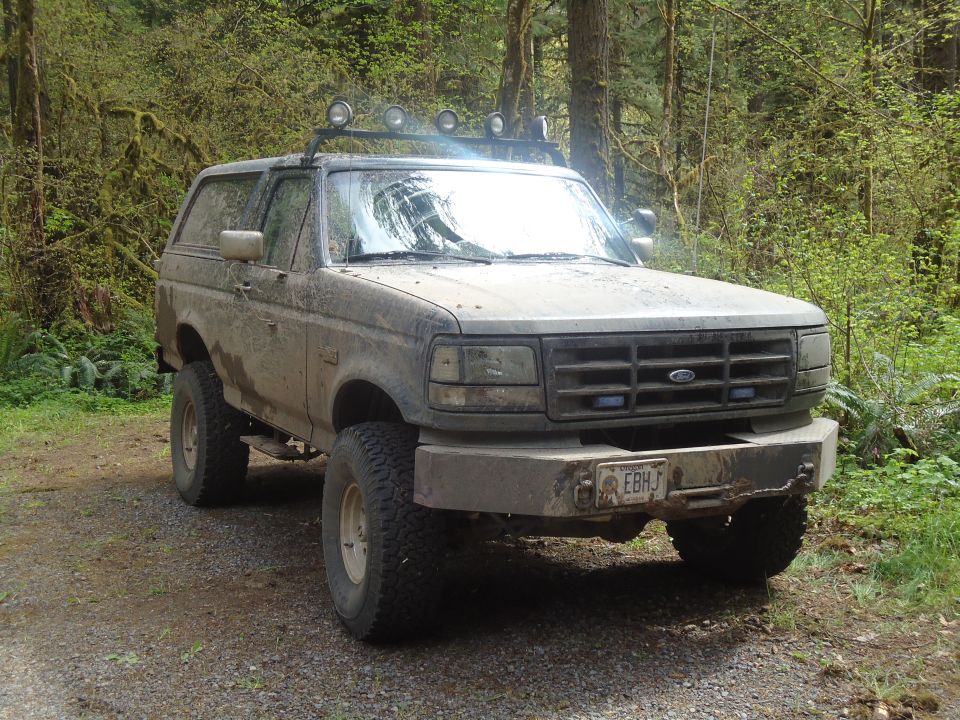 1995 Ford Bronco with off-road tires and roof lights parked on a dirt road
