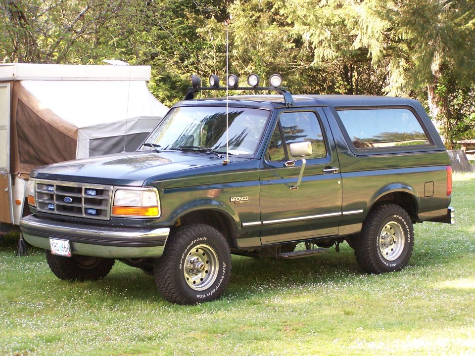 Dark green Ford Bronco parked on grass with a pop-up camper behind it