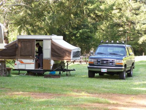 1995 Ford Bronco - A dark blue Ford Bronco is parked on a grassy area next to a pop-up camper.