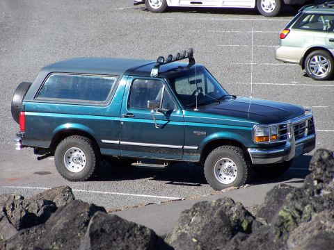 1995 Ford Bronco - A teal and black Ford Bronco is parked in a lot, with other vehicles visible in the background.