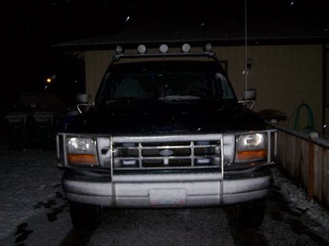 1995 Ford Bronco - A black Ford Bronco is parked outside in the snow at night, showing its front grille and light bar.