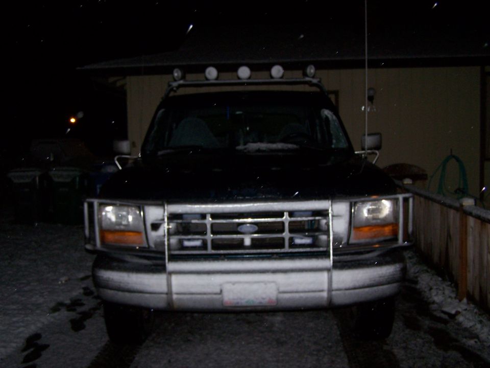Black Ford Bronco with a chrome grille and light bar, covered in snow
