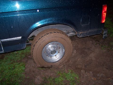 1995 Ford Bronco - A dark teal Ford Bronco is stuck in the mud, with its rear tire deep in the mire.