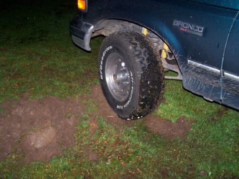 1995 Ford Bronco - A 1995 Ford Bronco XLT is stuck in the mud, with its front tire partially sunk into the wet ground.