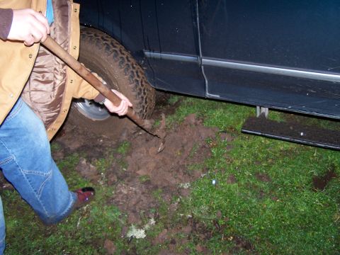 1995 Ford Bronco - A person uses a tool to dig mud from under the tire of a dark-colored SUV that is stuck in the ground.