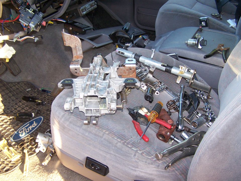 car interior with steering column parts and tools spread on seats and floor