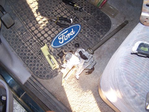 1995 Ford Bronco - Disassembled Ford steering column components and an emblem are scattered on the floor mat.