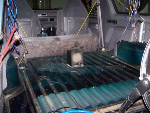 1995 Ford Bronco - The interior of a vehicle shows exposed wiring and a bare cargo area with a small speaker installed.
