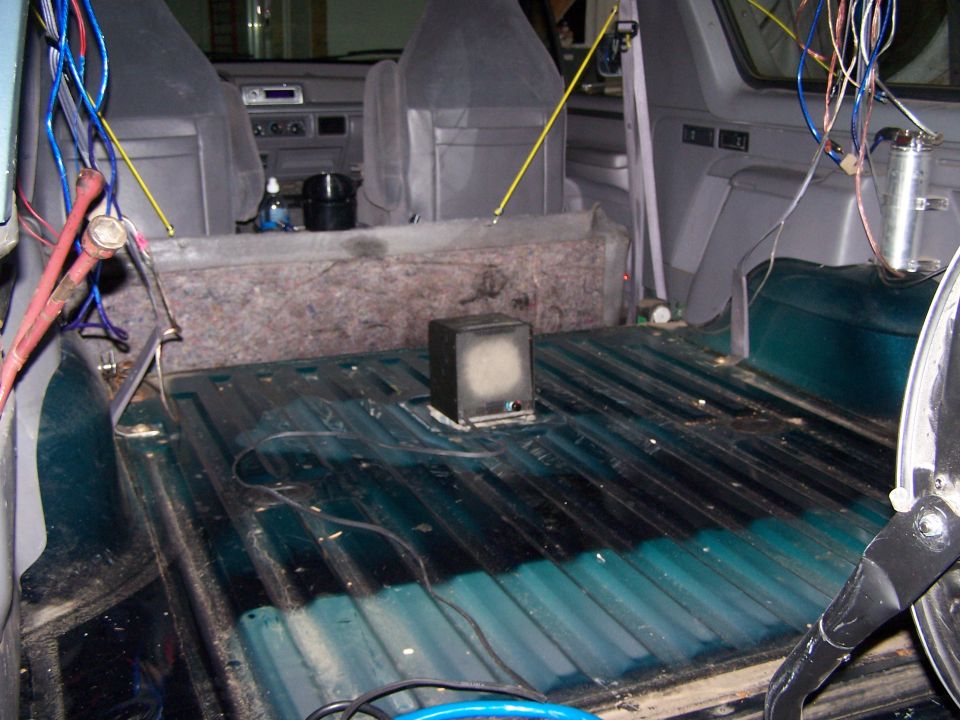 Vehicle interior with seats, dashboard, and a bare cargo area with lots of wires and a small speaker
