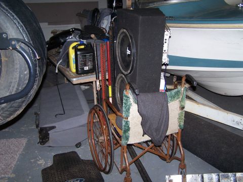 1995 Ford Bronco - A wheelchair is repurposed to hold subwoofers and other items, positioned near a boat on a trailer.