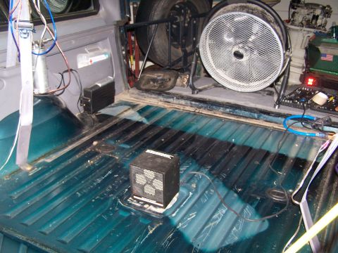 1995 Ford Bronco - The interior of a vehicle bed is shown with a large fan, a portable heater, and a spare tire mounted.