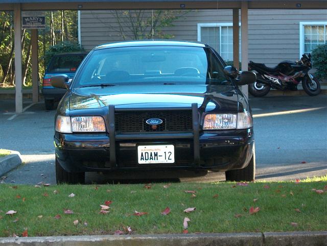 Front view of a black 2001 Ford Crown Victoria with a push bar and license plate ADAM-12
