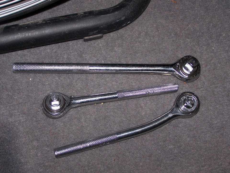 Three chrome ratchet wrenches on a dark surface. A black pipe is visible at the top
